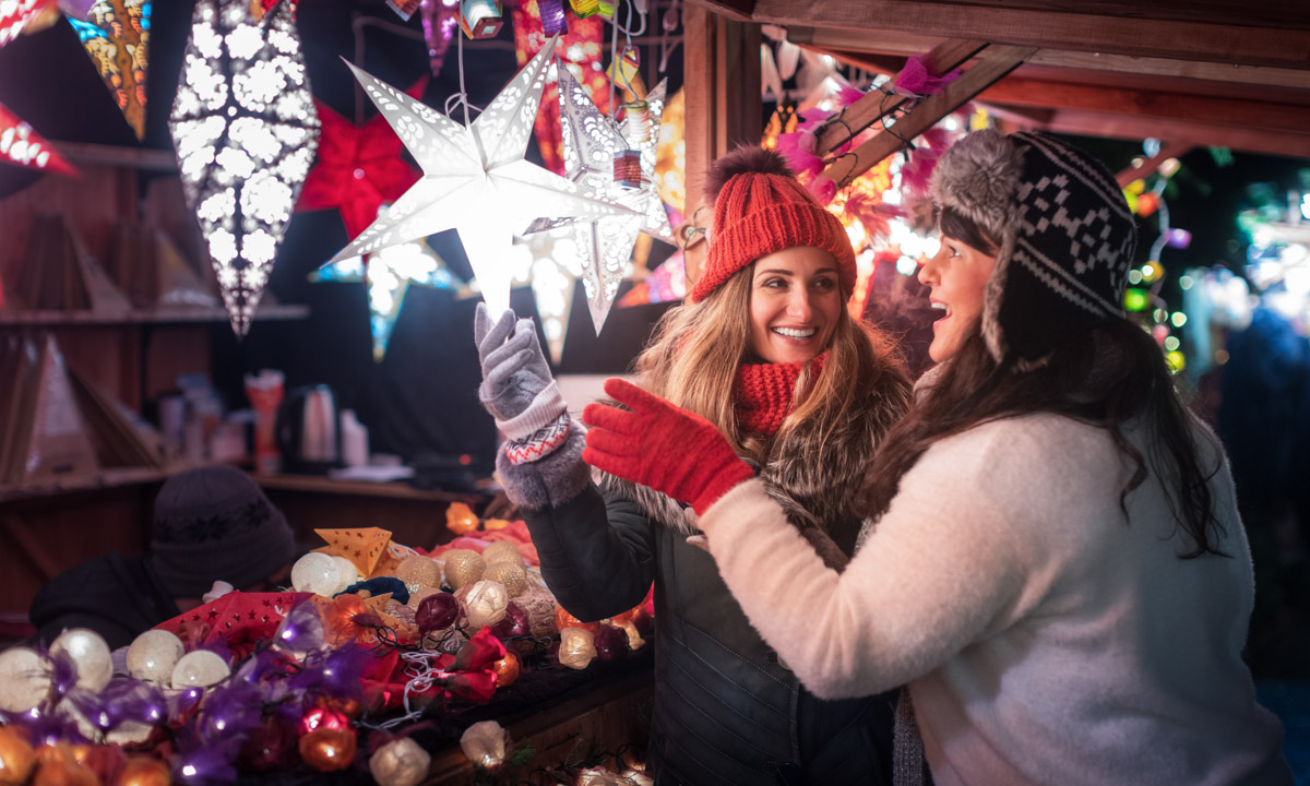 Two friends buying Christmas decoration on winter market booth